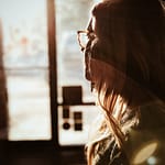 Side profile of a woman with long hair and glasses, illuminated by sunlight.