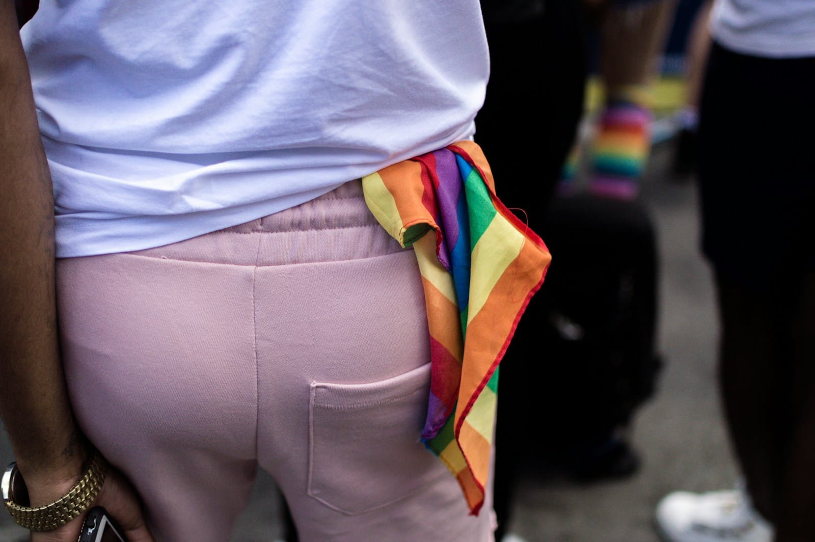 Individual wearing a rainbow bandana tied at the waist during a public event.