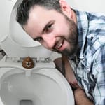 Man leaning over a toilet with a bidet attachment and a decorative item on the seat.