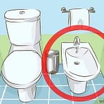 Illustration of a bidet and toilet setup in a bathroom with a towel rack.