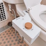 White bidet attachment with a wooden knob mounted on the side of a toilet.