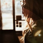 Side profile of a woman with long hair and glasses, illuminated by sunlight.