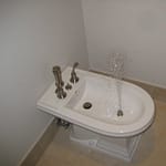 White bidet with water spraying from the nozzle in a bathroom setting.