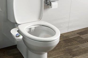 A white bidet toilet seat with a control panel on the side, positioned in a bathroom setting.