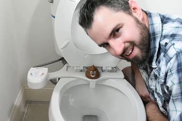 Man leaning over a toilet with a bidet attachment and a decorative item on the seat.