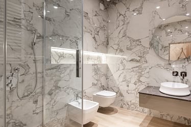Contemporary bathroom featuring marble walls, a round mirror, and modern fixtures.
