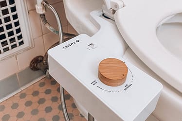 White bidet attachment with a wooden knob mounted on the side of a toilet.