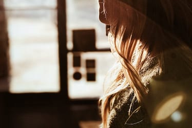 Side profile of a woman with long hair and glasses, illuminated by sunlight.