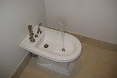 White bidet with water spraying from the nozzle in a bathroom setting.