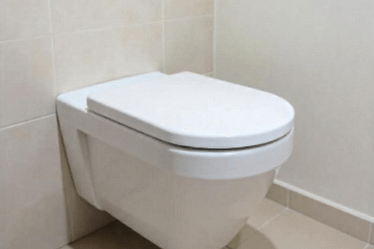 A modern wall-mounted toilet with a flush plate in a tiled bathroom setting.