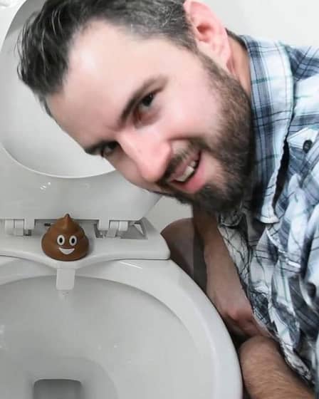 Man leaning over a toilet with a bidet attachment and a decorative item on the seat.