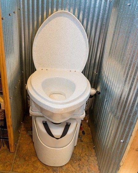 A waterless toilet installed in a bathroom with metal paneling and storage shelves.