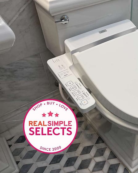 White bidet toilet seat with a control panel on the side in a bathroom setting.