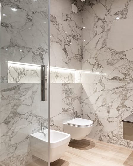 Contemporary bathroom featuring marble walls, a round mirror, and modern fixtures.