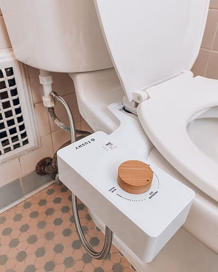 White bidet attachment with a wooden knob mounted on the side of a toilet.