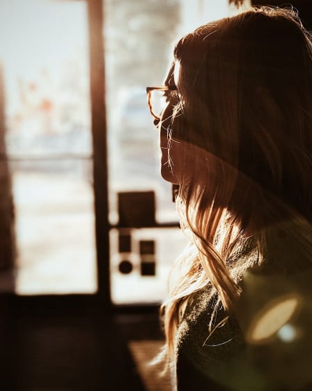 Side profile of a woman with long hair and glasses, illuminated by sunlight.