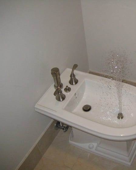 White bidet with water spraying from the nozzle in a bathroom setting.