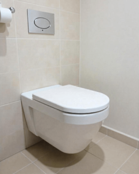 A modern wall-mounted toilet with a flush plate in a tiled bathroom setting.