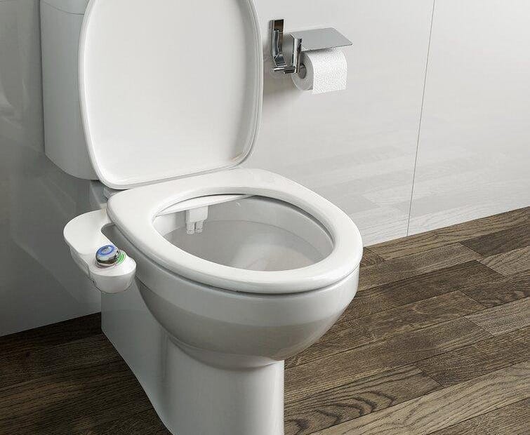A white bidet toilet seat with a control panel on the side, positioned in a bathroom setting.