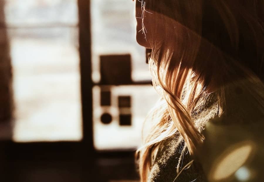 Side profile of a woman with long hair and glasses, illuminated by sunlight.