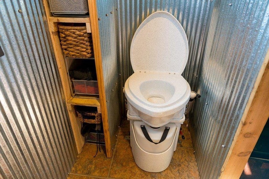 A waterless toilet installed in a bathroom with metal paneling and storage shelves.