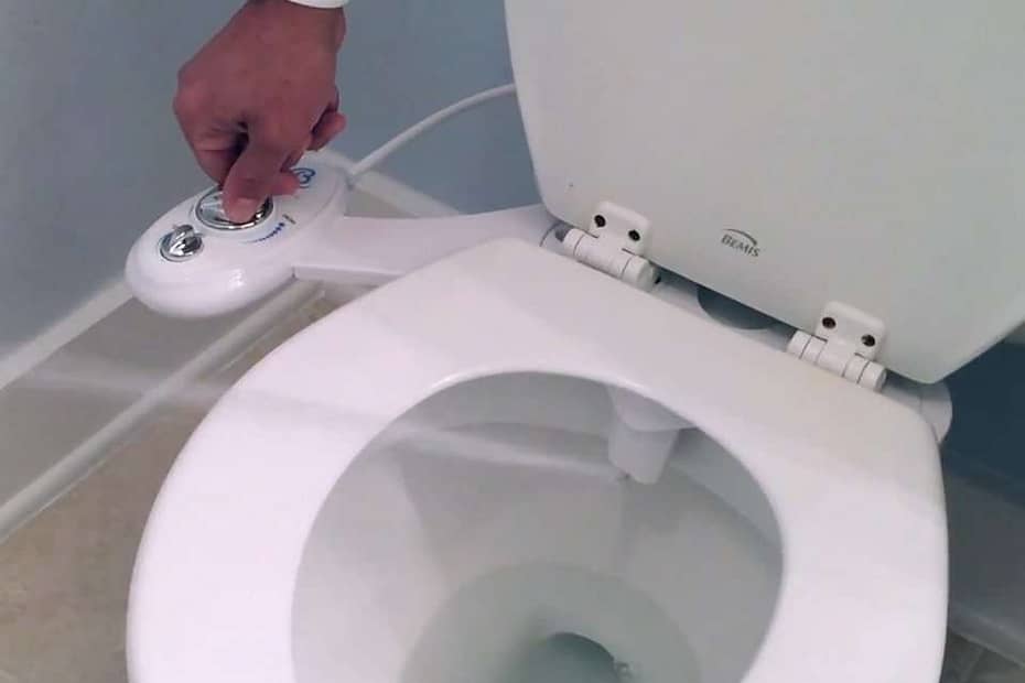Hand operating the control panel of a bidet attachment on a toilet.