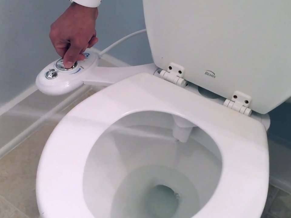 Hand operating the control panel of a bidet attachment on a toilet.