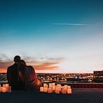 couple sitting on the field facing the city