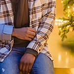 Two individuals sitting closely together, one wearing a plaid jacket and the other in a gray coat.