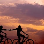 woman on bike reaching for man's hand behind her also on bike