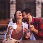 Young couple sitting at a cafe, laughing and enjoying each other's company while holding a cup and a bottle.