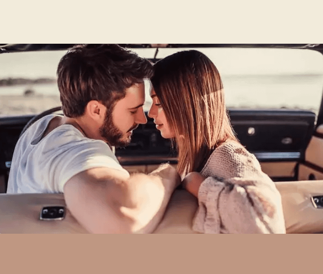 Young couple leaning towards each other inside a car with a scenic background.