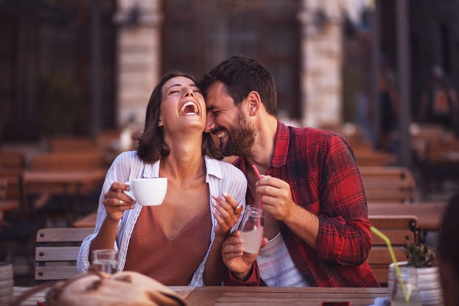 Young couple sitting at a cafe, laughing and enjoying each other's company while holding a cup and a bottle.